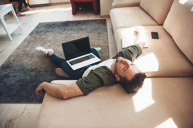Mann liegt mit einem Laptop auf dem Boden und schläft, weil sein Laptop langsam ist. Bild: stock.adobe.com/Strelciuc (https://stock.adobe.com/de/images/tired-caucasian-man-lying-on-floor-with-a-laptop-falling-asleep-after-working-online/355364284?asset_id=355364284)