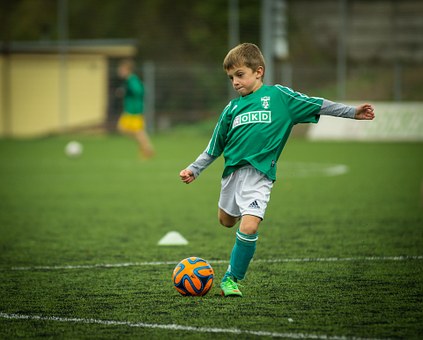 Ein kleiner Junge im grünen Trikot auf dem Fußballplatz setzt gerade an, einen Ball zu schießen. Foto: Pixabay