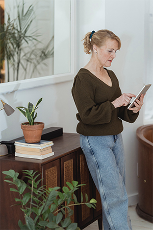 Frau, an Kommode gelehnt mit Tablet in der Hand überprüft App-Berechtigungen. Bild: Pexels/Teona Swift