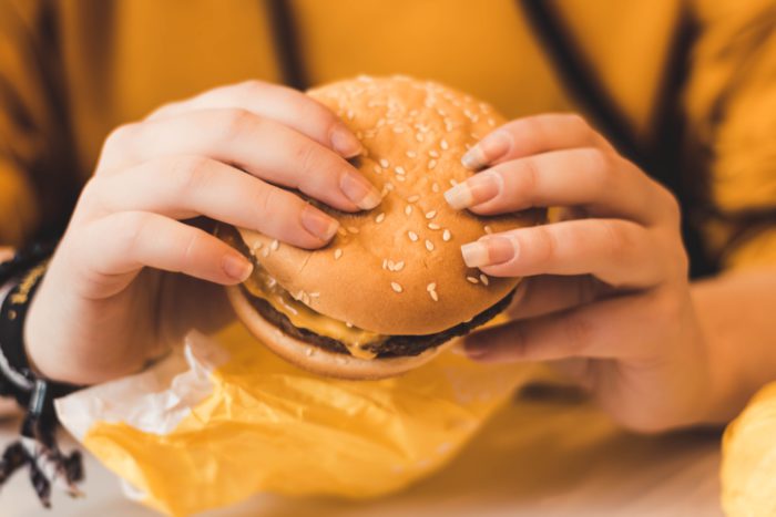 Eine Person hält einen Burger in den Händern, den sie sich vielleicht mit Mecces-Coupons geholt hat. Bild: Unsplash/Christian Wiediger