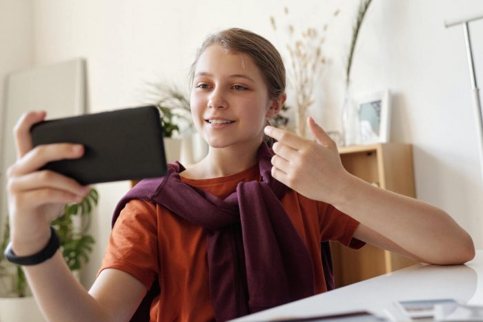 Mädchen sitzt an einem Tisch und telefoniert via Video. Bild: Pexels/JuliaMCameron