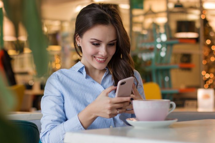 WhatsApp: Nachrichten verschwinden. Junge Frau im Café mit Handy in der Hand, lächelt. Bild: Pixabay