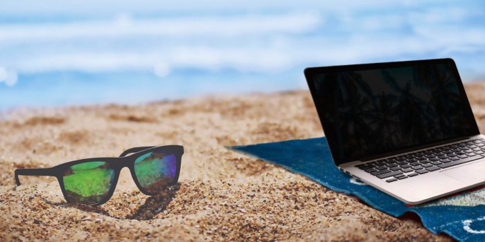 Workation: Laptop und Sonnenbrille liegen am Strand. Im Hintergrund das Meer. Bild: Pixabay