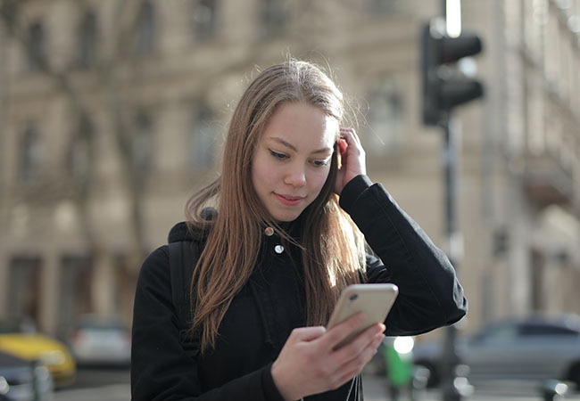 Telefonat aufnehmen: Junge Frau schaut unterwegs auf Ihr Handy. Bild: Pexels/Andrea Piacquadio