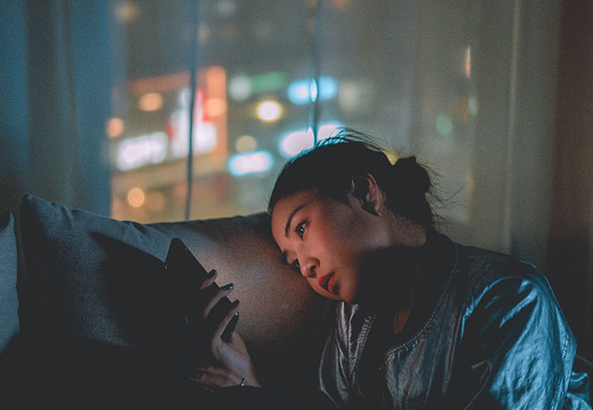 Cell Broadcast: Junge Frau im Dunkeln auf dem Sofa blickt auf ihr Handy. Bild: Pexels/Mikotoraw