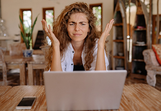 GriftHorse: Frau am Laptop mit Handy auf dem Schreibtisch ärgert sich. Bild: Pexels/Yan Krukov