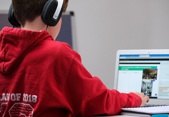 Medienkompetenz: Junge im roten Pulli mit Kopfhörern vorm Laptop. Bild: Unsplash/Compare Fibre