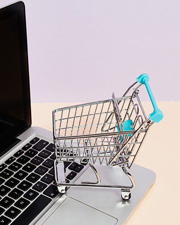 Mit PayPal bezahlen: Aufgeklapptes Laptop und kleiner Einkaufswagen symbolisieren das Einkaufen. Bild: Pexels/Karolina Grabowska