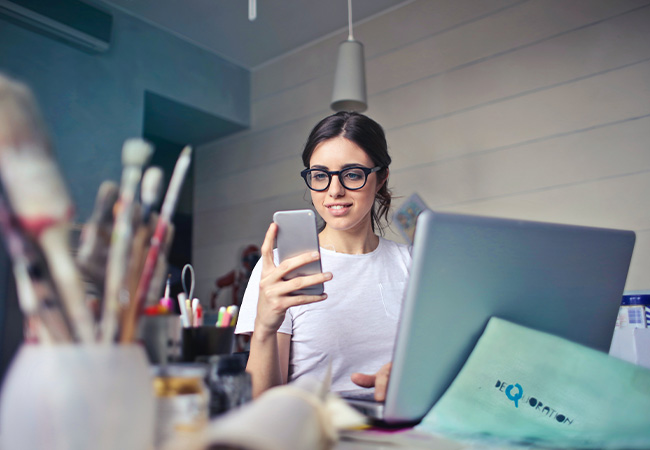 Arbeitszeiterfassung. Junge Frau im Home Office blickt auf ihr Handy. Bild: Pexels/Andrea Piacquadio
