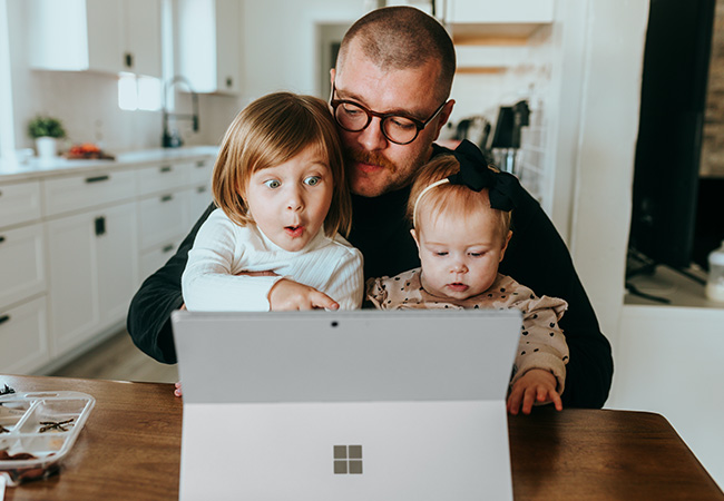 Virtuelle Konferenz: Mann sitzt mit zwei Kleinkindern vor einem Surface. Bild: Unsplash/Surface