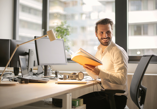 DEX: Mann mit Heft in der Hand am digitalen Arbeitsplatz. Bild: Pexels/Andrea Piacquadio