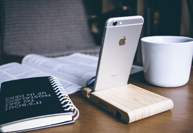 Daten synchronisieren: Silbernes iPhone in einem hölzernen Halter auf einem Schreibtisch. Bild: Unsplash/freestocks