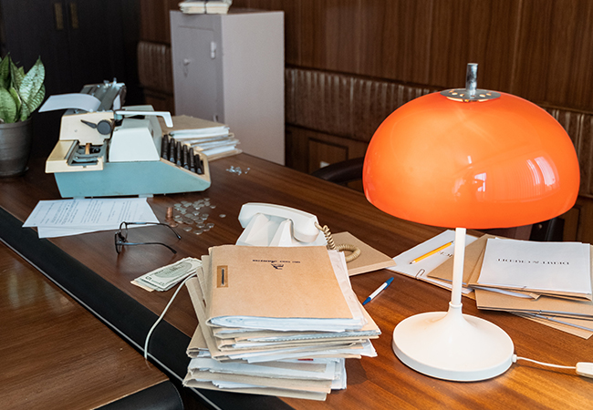 Digitales Büro: Schreibtisch mit Schreimaschine, altem Telefon, Aktenbergen und orange-farbener Lampe. Bild: Pexels/Mart Production