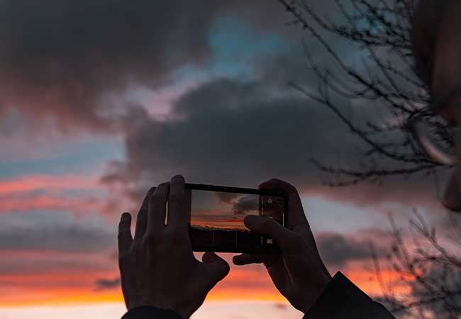 Mein Google-Konto: Zwei Hände halten ein Handy und nehmen ein Foto des Sonnenuntergangs auf. Bild: Pexels/Irina Iriser