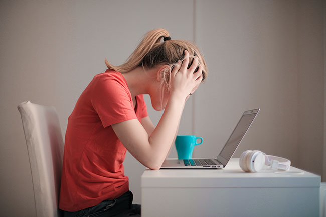 Phishing-Betrug: Frau in rotem Shirt schaut auf Laptop, Hände raufen die Haare. Bild: Pexels/Andrea Piacquadio