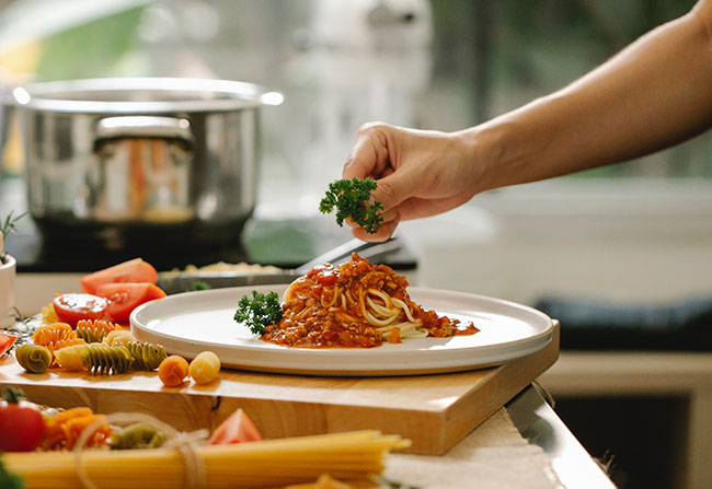 Addons: Jemand garniert Spaghetti mit Petersilie. Bild: Pexels/Klaus Nielsen