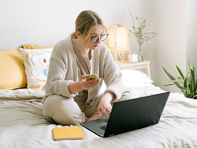 MFA-Fatigue-Angriff: Frau auf Bett mit Laptop und Handy. Bild: Pexels/Ivan Samkov
