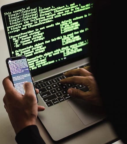 Ransom Cartel: Nicht erkennbarer Hacker mit Smartphone; Eingabe auf Laptop am Schreibtisch. Bild: Pexels/Sora Shimazaki