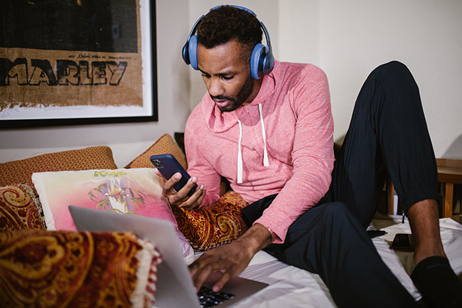 Zwei-Faktor-Authentifizierung: Mann mit Kopfhörern am Laptop mit Handy in der Hand. Bild: Pexels/RODNAE Productions