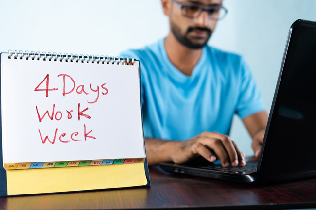 Konzept einer Vier-Tage-Woche mit einem jungen Mann, der im Hintergrund arbeitet und den Kalender zeigt. Bild: ©WESTOCK/stock.adobe.com