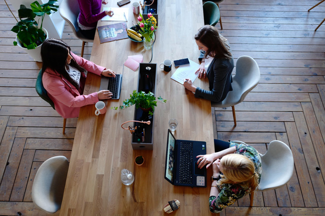 Büro 4.0: Draufsicht auf drei Frauen an einem Tisch mit unterschiedlichen Arbeitsmaterialien. Bild: Pexels/@cowomen-1058097