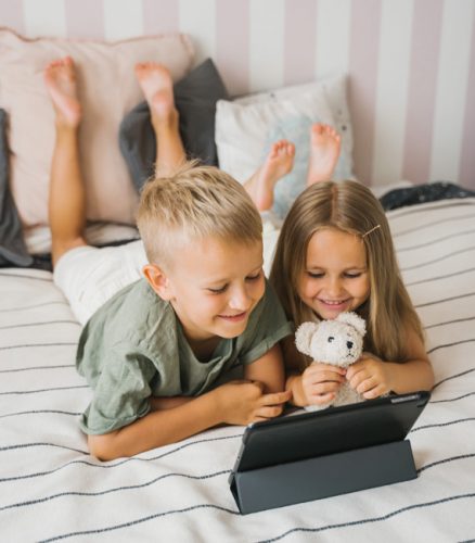 Ein Junge und ein Mädchen liegen auf dem Bett und schauen fröhlich auf ein Tablet. Bild: Pexels/Tima Miroshnichenko (https://www.pexels.com/de-de/foto/jungen-und-madchen-sitzen-auf-dem-bett-4908507/)