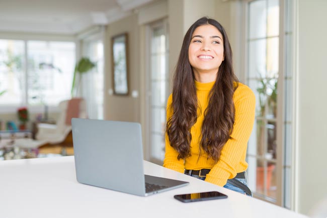 Junge Frau wendet Blick fröhlich vom Laptop ab. Bild: stock.adobe.com/Krakenimages.com (https://stock.adobe.com/de/images/young-woman-using-computer-laptop-looking-away-to-side-with-smile-on-face-natural-expression-laughing-confident/261974048?asset_id=261974048)