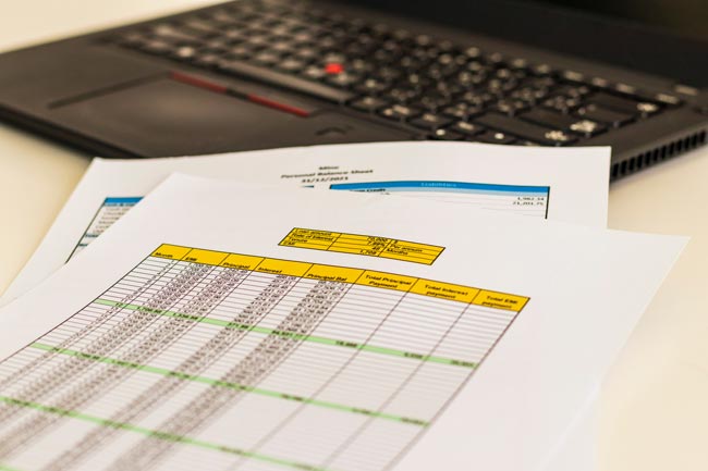 Excel-Funktion: aufgeklappter Laptop, Papier mit Tabellen. Bild: stock.adobe.com/Four_Lakes (https://stock.adobe.com/de/images/close-up-shot-of-a-print-outs-of-excel-table-of-a-bank-loan-amortization-table-personal-balance-sheet-and-laptop-banking/528042717?asset_id=528042717)