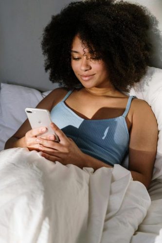 iPhone-Screenshot: Junge schwarze Frau mit ihrem iPhone im Bett. Bild: Pexels/cotonbro studio (https://www.pexels.com/de-de/foto/frau-apple-apfel-iphone-4046303/)