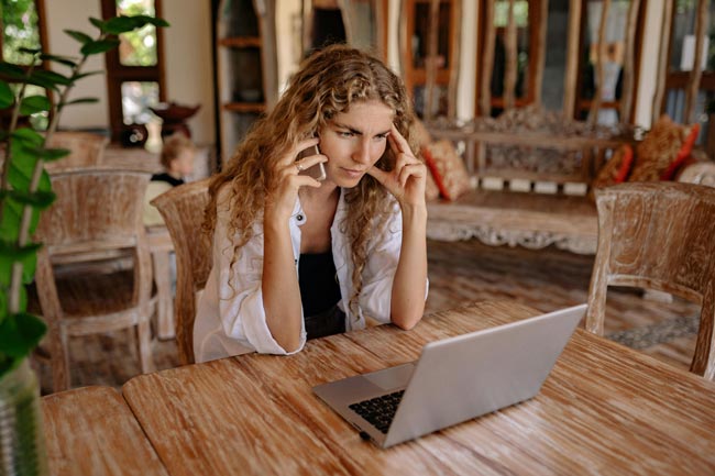 Rufnummer blockieren: Frau blickt ernst in ihr Laptop, Handy am Ohr. Bild: Pexels/Yan Krukau (https://www.pexels.com/de-de/foto/frau-smartphone-laptop-arbeiten-4458396/)