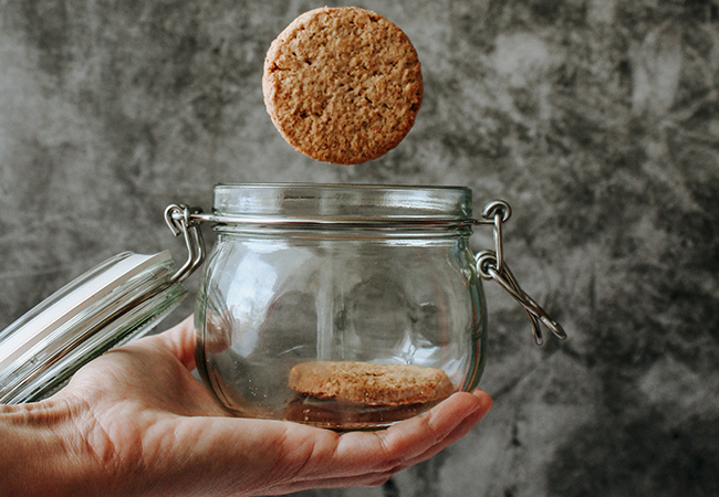 Cookies verwalten – Hand hält Glas mit Keks, ein weiterer fällt ins Glas. Bild: Unsplash/Tijana-Drndarski
