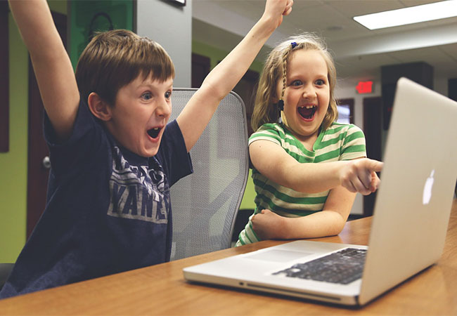 Das Bild zeigt zwei Kinder, die vor einem Computer sitzen und sich freuen. Bild: Pixabay