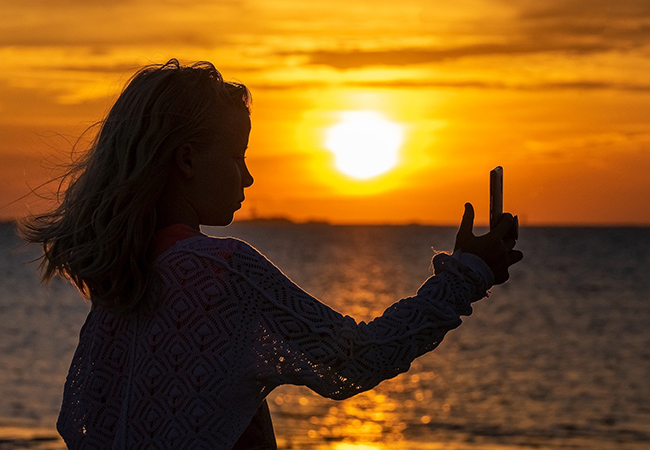 Kinder-Selfies: Mädchen am Strand mit Handy in der Hand vor Sonnenuntergang. Bild: Pixabay