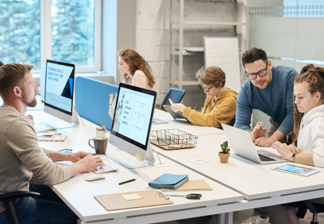 Home Office versus Büroalltag - fünf Arbeitnehmer an einer Tischgruppe mit Computerausstattung. Bild: Pexels/fauxels